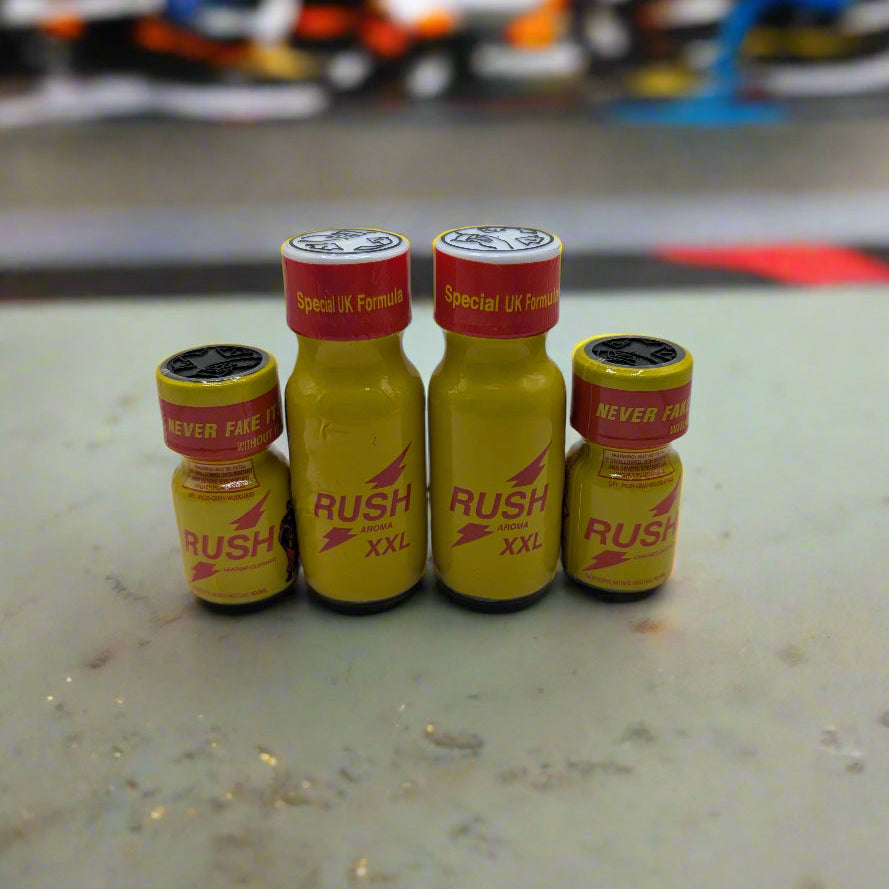 Four yellow bottles of 'Rush' poppers, two small and two larger, displayed on a surface with a blurred background.