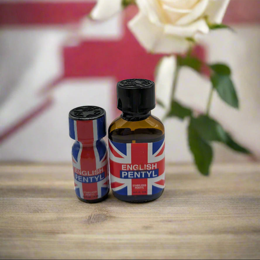 Two bottles of English Pentyl poppers, one small and one large, with Union Jack branding, placed on a wooden surface with a blurred background featuring a British flag and a rose.