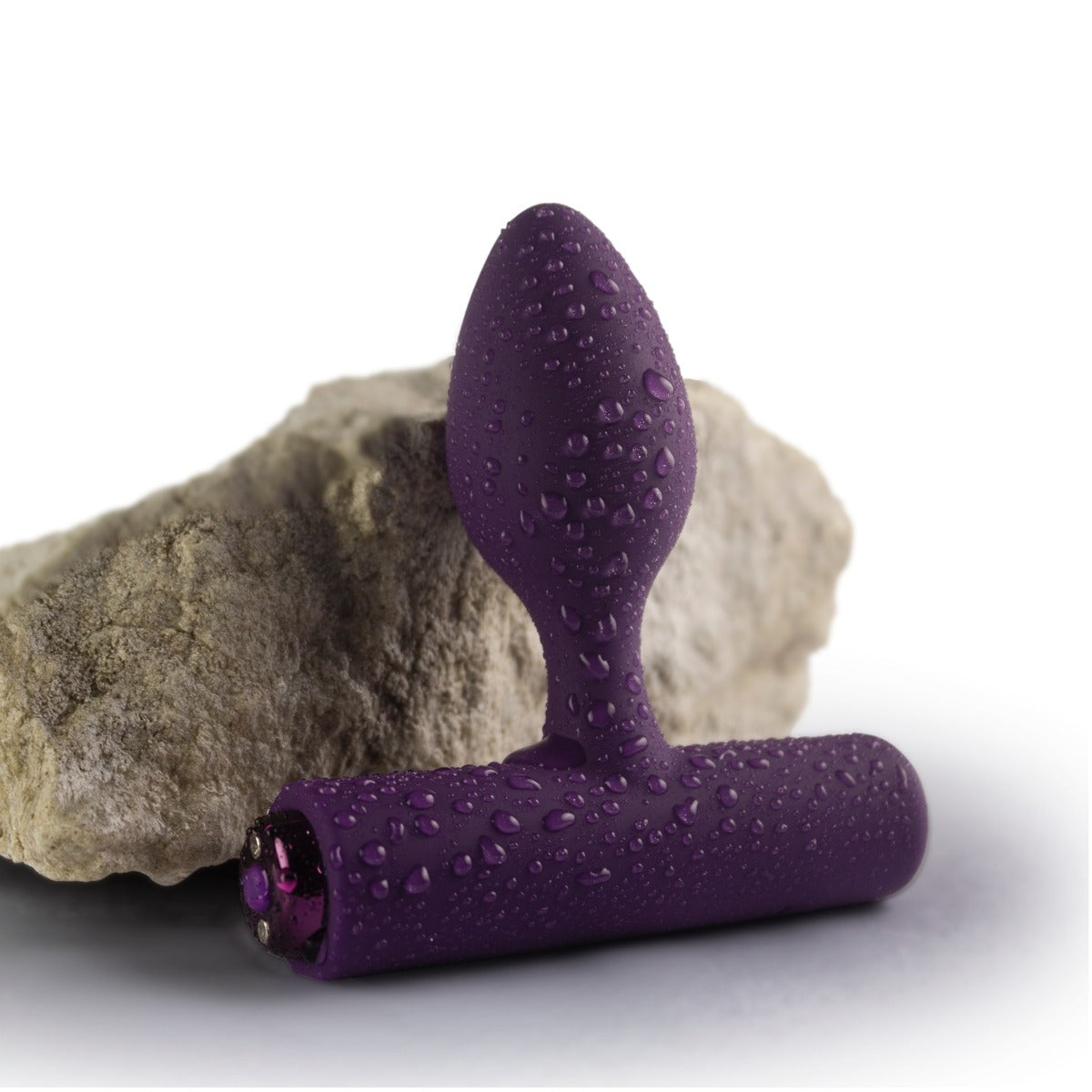 Rocks Off Solaris Rechargeable Plug Purple next to rock with drops of water